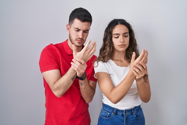 Young hispanic couple standing over isolated background suffering pain on hands and fingers, arthritis inflammation