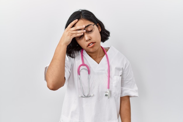 Young hispanic doctor woman wearing stethoscope over isolated background tired rubbing nose and eyes feeling fatigue and headache. stress and frustration concept.