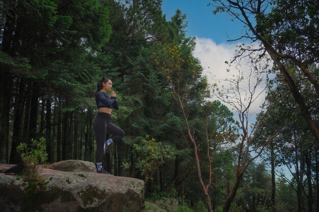 A Young Hispanic female practicing yoga on a cliff in a forest