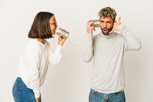 Giovani amici ispanici che parlano attraverso un sistema di barattoli di latta che mostra un gesto di telefonata con le dita.