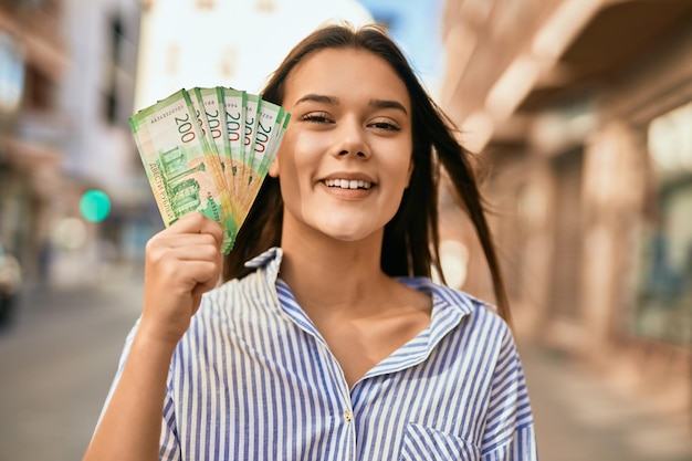 Фото Молодая латиноамериканская девушка счастливо улыбается, держа банкноты российского рубля в городе.