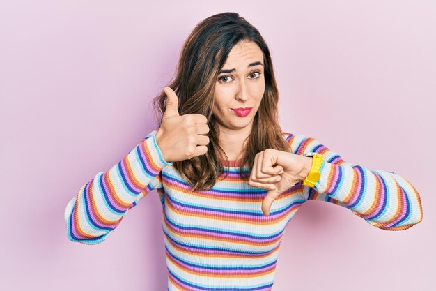 Young hispanic girl wearing casual clothes doing thumbs up and down, disagreement and agreement expression. crazy conflict