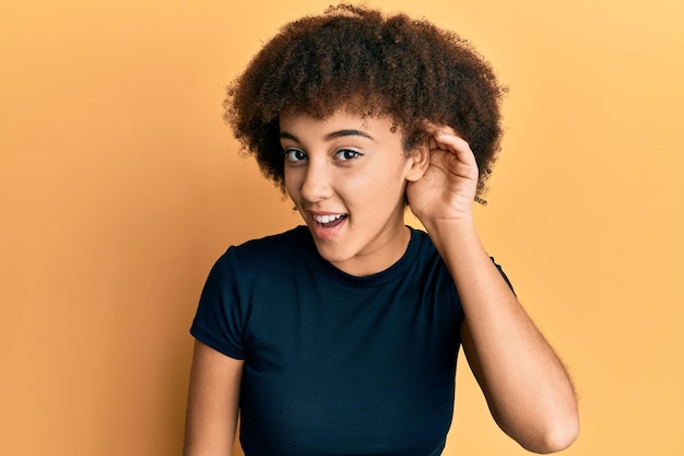 Молодая латиноамериканская девушка в повседневной одежде улыбается, прикрывая ухо рукой, слушая и слушая слухи или сплетни. концепция глухоты.