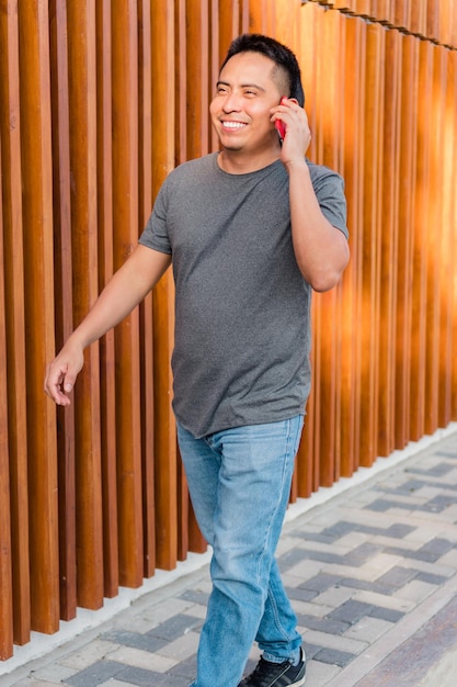 Young Hispanic indigenous man walking down the street while talking on cell phone