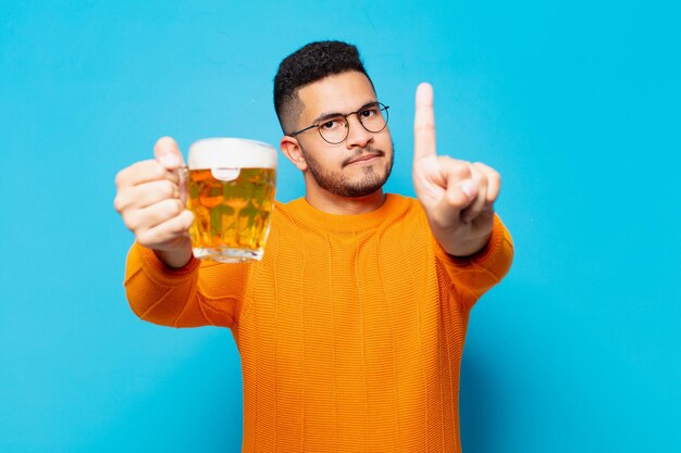 Young hispanic man angry expression and holding a beer