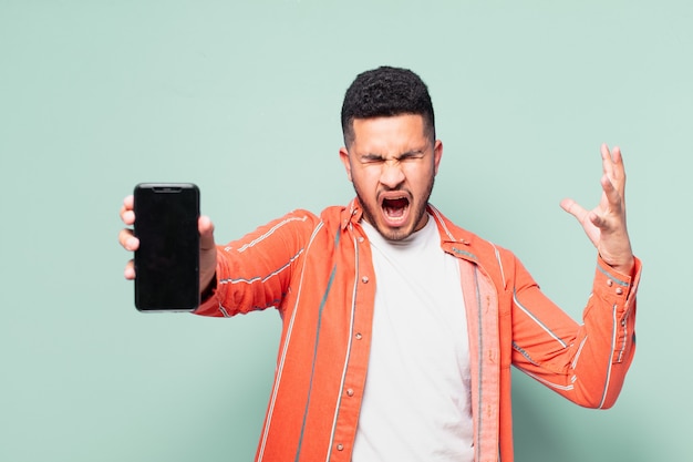 Young hispanic man angry expression and holding a mobile phone