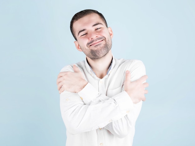 Young hispanic man in casual clothes hugs himself happy and positive, smiling confidently. self-love and self-care