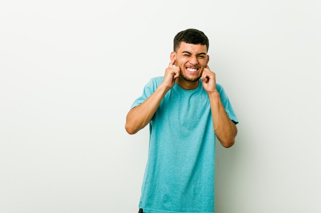 Young hispanic man covering ears with hands.