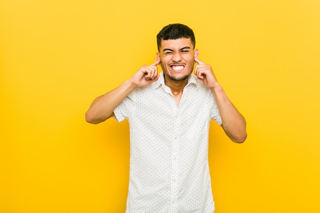Young hispanic man covering ears with hands.