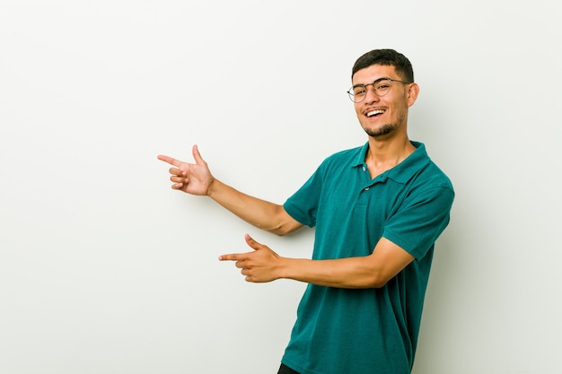 Young hispanic man excited pointing with forefingers away.