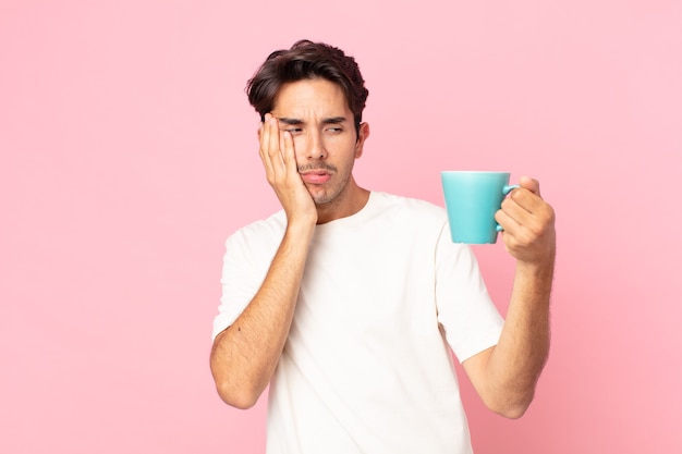 Young hispanic man feeling bored, frustrated and sleepy after a tiresome and holding a coffee mug