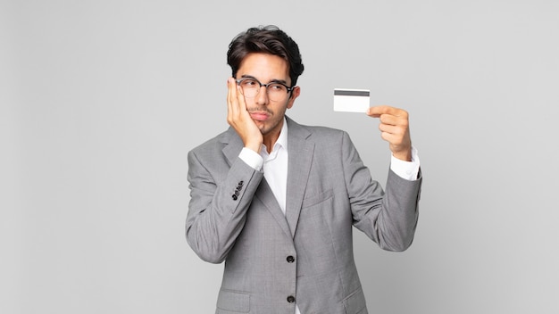 young hispanic man feeling bored, frustrated and sleepy after a tiresome and holding a credit card