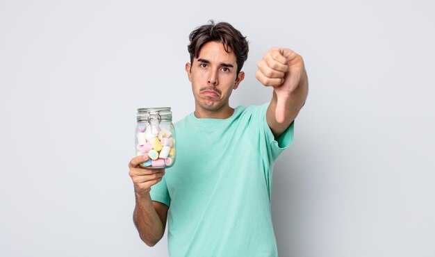 Young hispanic man feeling cross,showing thumbs down. jelly candies concept