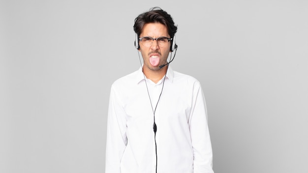Young hispanic man feeling disgusted and irritated and tongue out. telemarketer concept