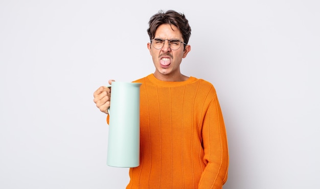 Young hispanic man feeling disgusted and irritated and tongue out. thermos concept