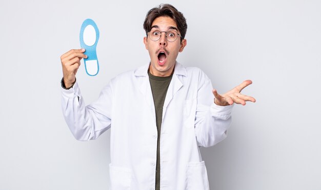 Young hispanic man feeling extremely shocked and surprised. chiropodist concept