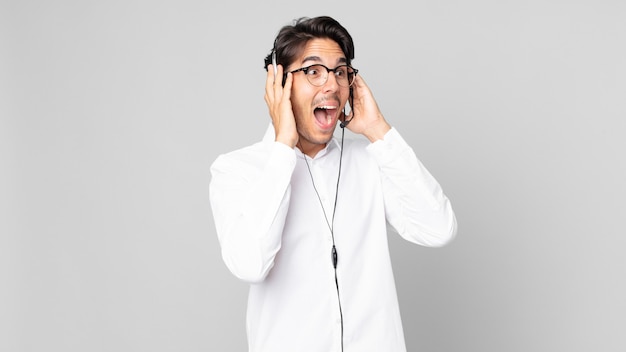 Young hispanic man feeling happy, excited and surprised. telemarketer concept