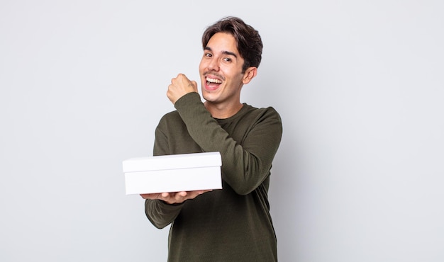 Young hispanic man feeling happy and facing a challenge or celebrating. white box concept