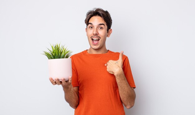 Young hispanic man feeling happy and pointing to self with an excited. decorative plant concept