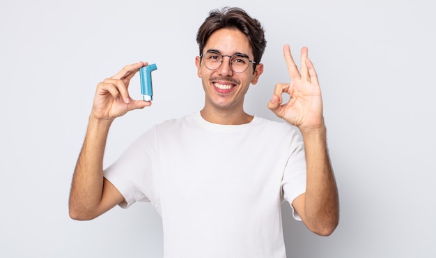 Young hispanic man feeling happy, showing approval with okay gesture. asthma concept