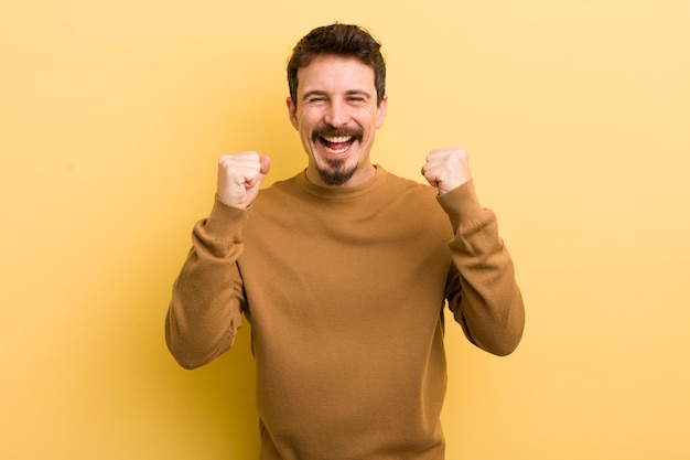 Young hispanic man feeling happy surprised and proud shouting and celebrating success with a big smile