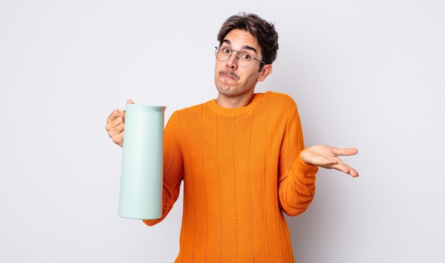 Young hispanic man feeling puzzled and confused and doubting. thermos concept