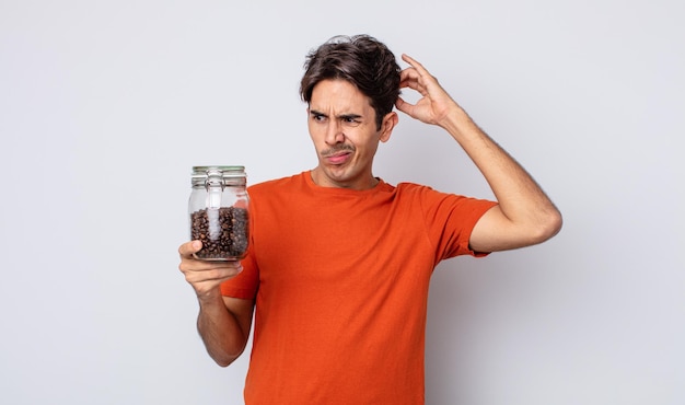 Young hispanic man feeling puzzled and confused, scratching head. coffee beans concept