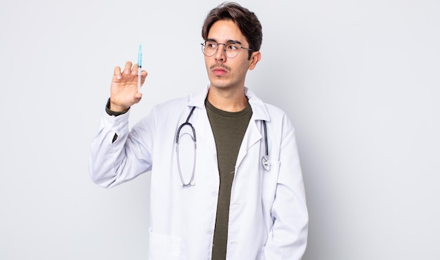 Young hispanic man feeling sad, upset or angry and looking to the side. doctor syringe concept