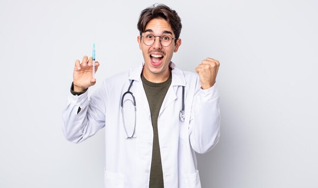 Young hispanic man feeling shocked,laughing and celebrating success. doctor syringe concept