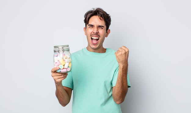 Young hispanic man feeling shocked,laughing and celebrating success. jelly candies concept