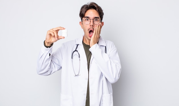 young hispanic man feeling shocked and scared. physician with pills bottle concept