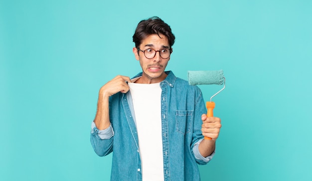 Young hispanic man feeling stressed anxious tired and frustrated and holding a paint roller