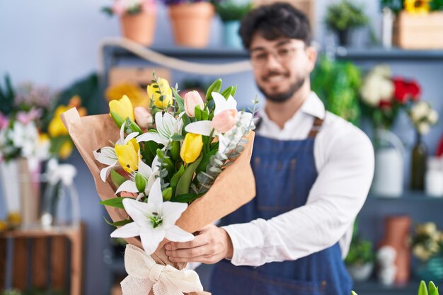 Young hispanic man florist holding bouquet of flowers at florist shop