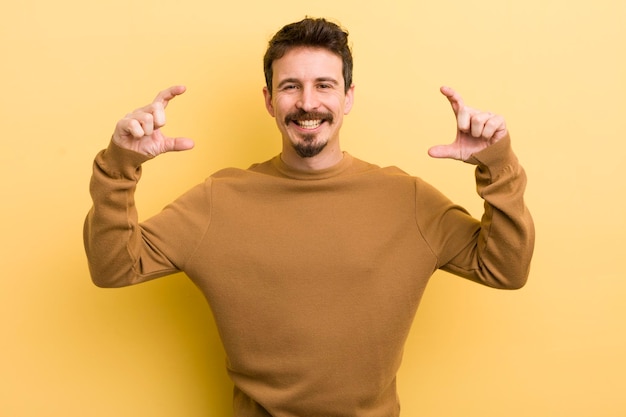 Young hispanic man framing or outlining own smile with both hands looking positive and happy wellness concept