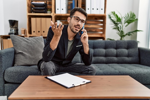 Young hispanic man having psychology session talking on the smartphone at clinic