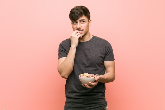 Young hispanic man holding a cereal bowl relaxed thinking about something