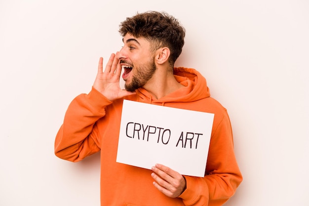 Young hispanic man holding a crypto art placard isolated on white background shouting and holding palm near opened mouth