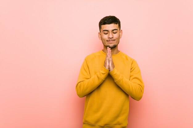 Young hispanic man holding hands in pray near mouth, feels confident.