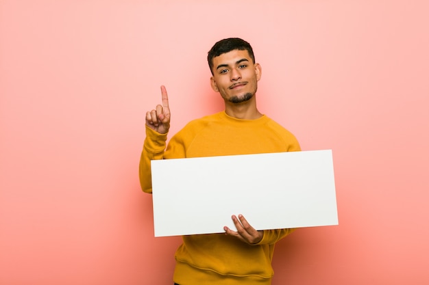 Young hispanic man holding a placard