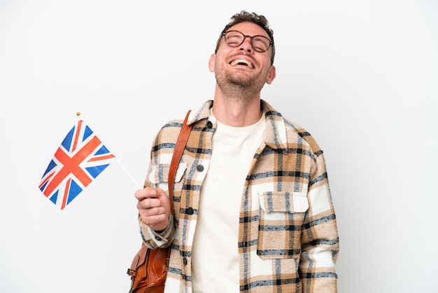 Young hispanic man holding an United Kingdom flag isolated on white background laughing