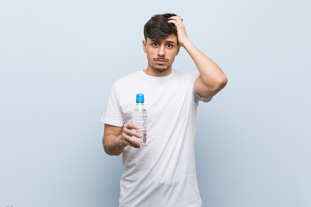 Young hispanic man holding a water bottle being shocked, she has remembered important meeting.