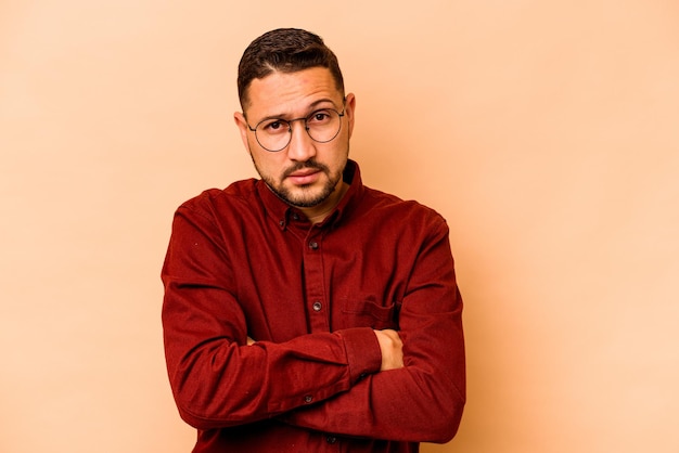 Young hispanic man isolated on beige background suspicious uncertain examining you