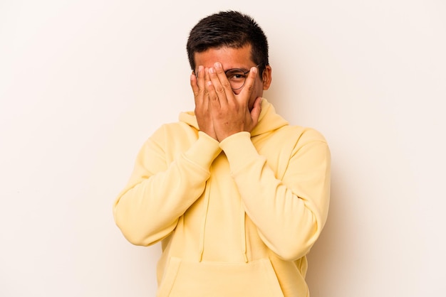 Young hispanic man isolated on white background blink through fingers frightened and nervous