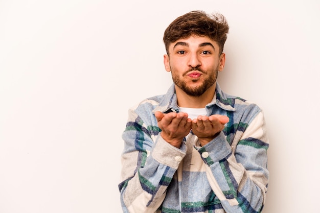 Young hispanic man isolated on white background folding lips and holding palms to send air kiss