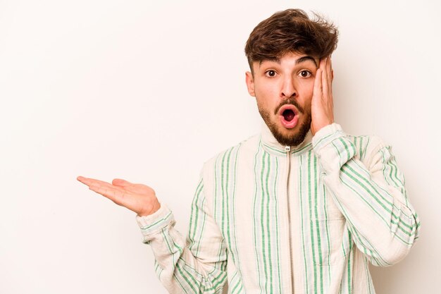 Young hispanic man isolated on white background impressed holding copy space on palm