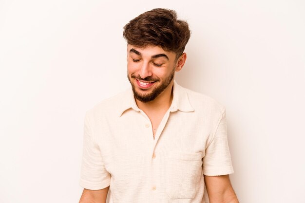 Young hispanic man isolated on white background laughs and closes eyes feels relaxed and happy