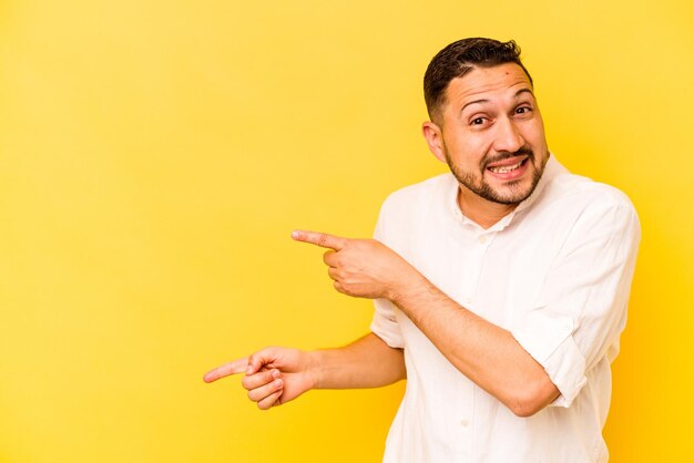 Young hispanic man isolated on yellow background excited pointing with forefingers away