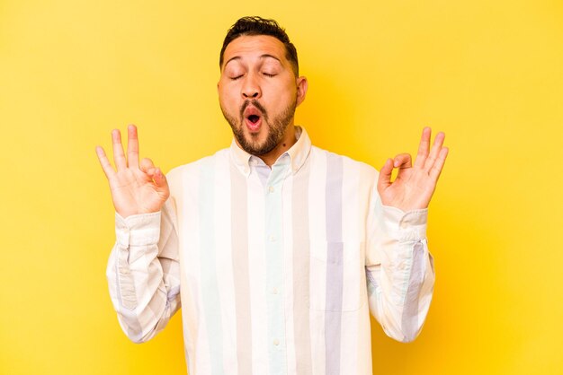 Young hispanic man isolated on yellow background relaxes after hard working day she is performing yoga