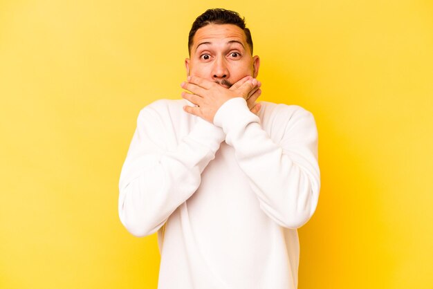 Young hispanic man isolated on yellow background shocked covering mouth with hands