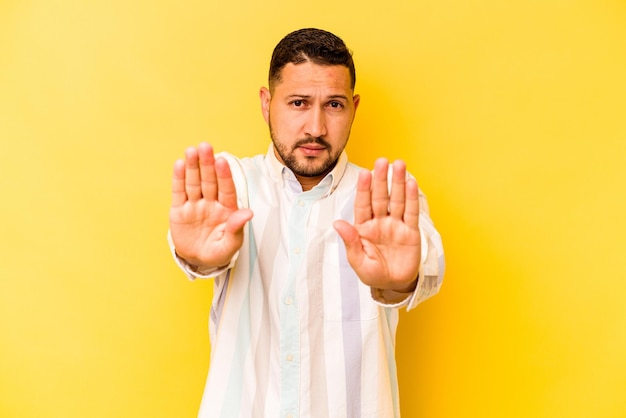 Young hispanic man isolated on yellow background standing with outstretched hand showing stop sign preventing you